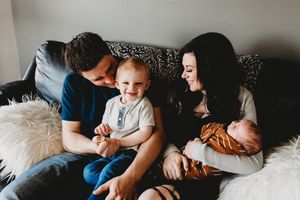 Happy family with toddler and newborn baby sitting together on a cozy couch.