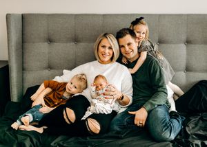 Happy family with parents and three young children sitting together on a bed smiling.