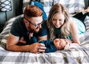 Happy couple lying on a bed smiling at their newborn baby in a cozy bedroom setting.