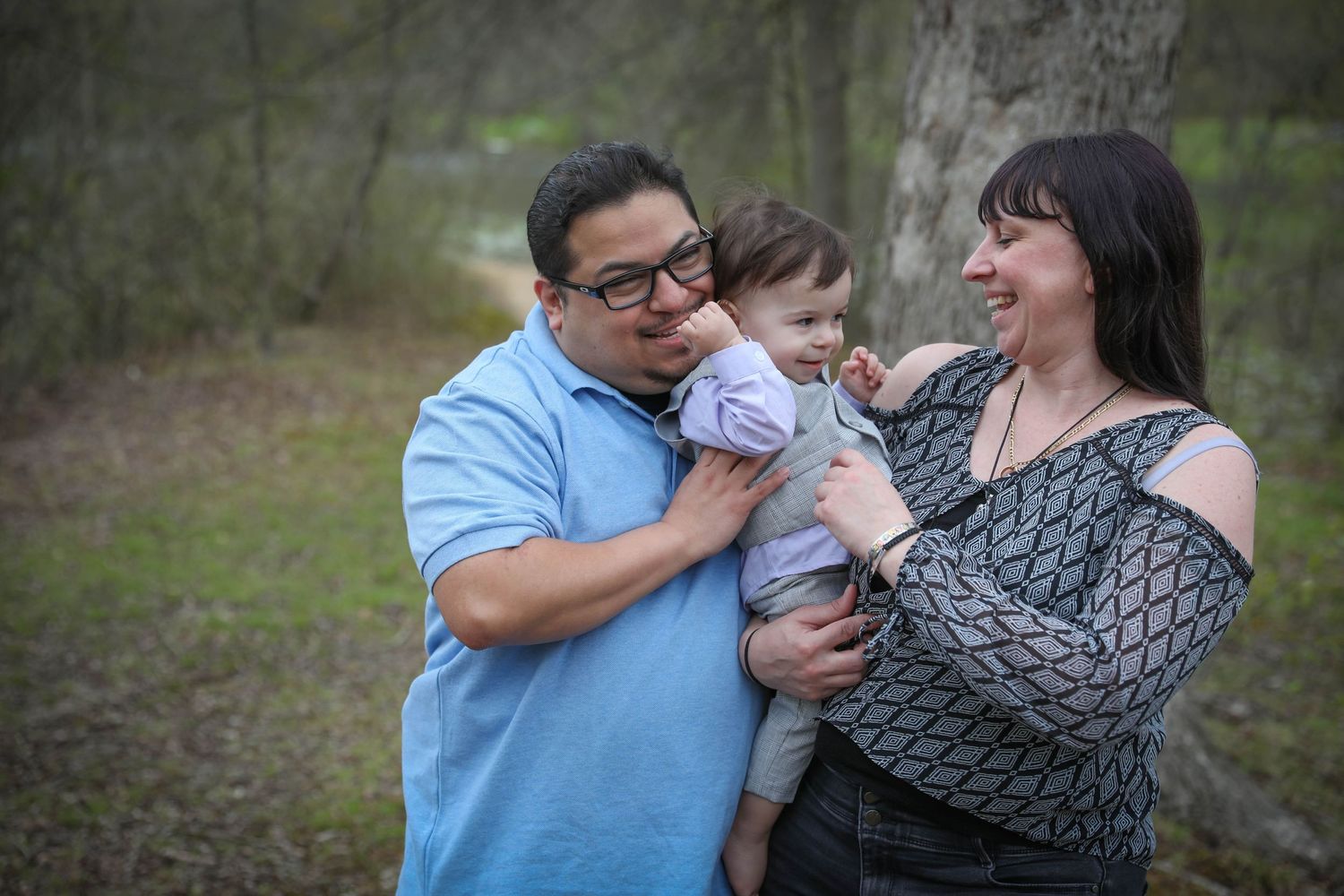Family shares a tender moment together outdoors while holding a baby in casual attire. Family photoshoot. L. Visions Photography.