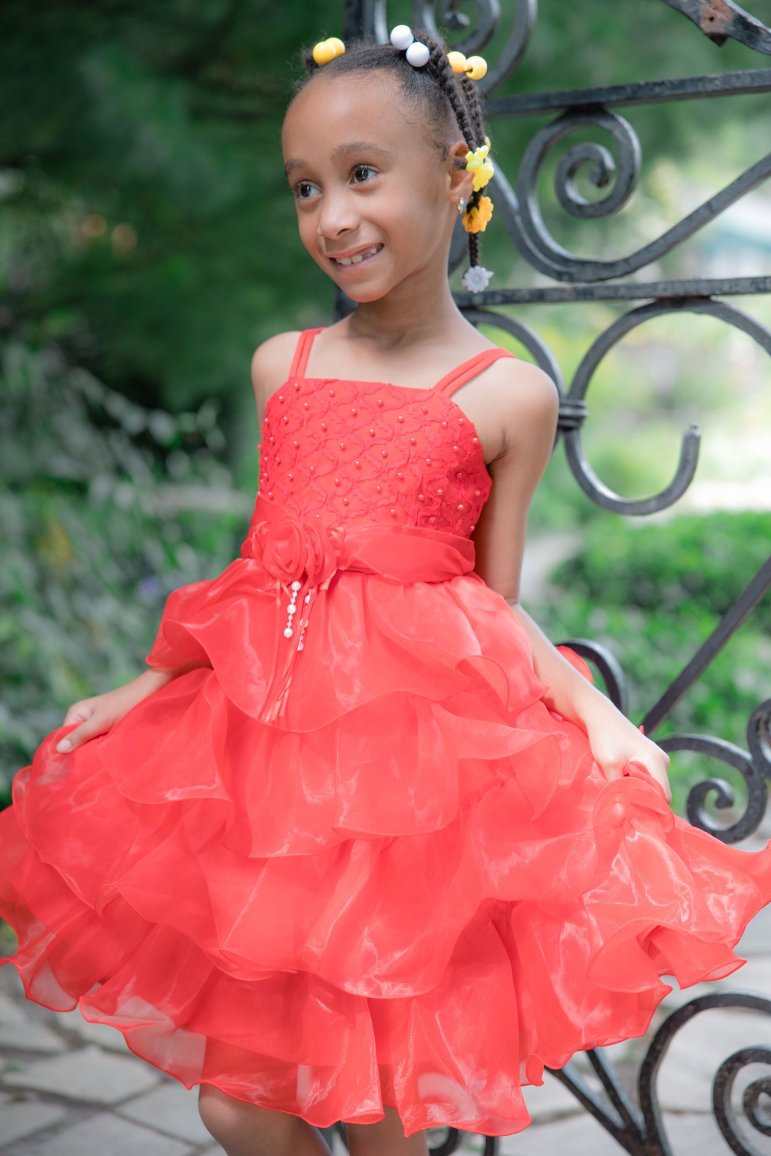Child wearing bright red ruffled party dress poses by ornate iron gate. Lifestyle photoshoot. L. Visions Photography