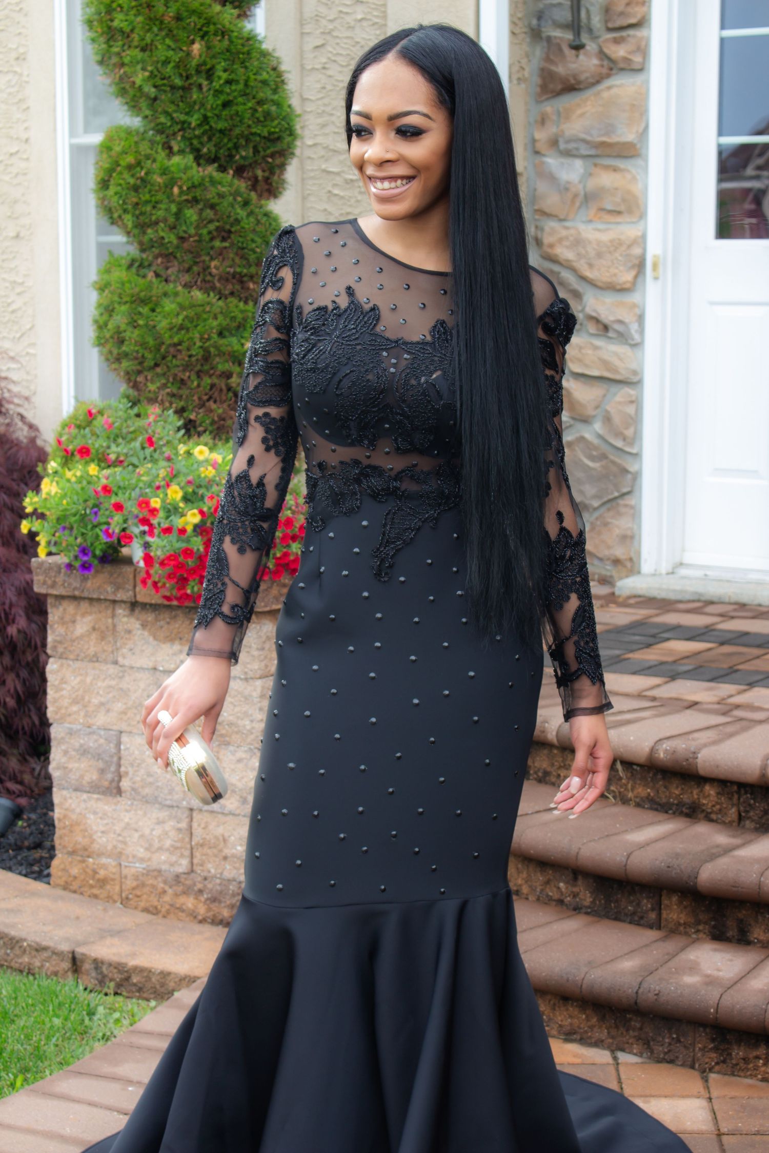 Woman in elegant black lace mermaid gown poses on stone steps with floral decorations. Prom photoshoot. L. Visions Photography
