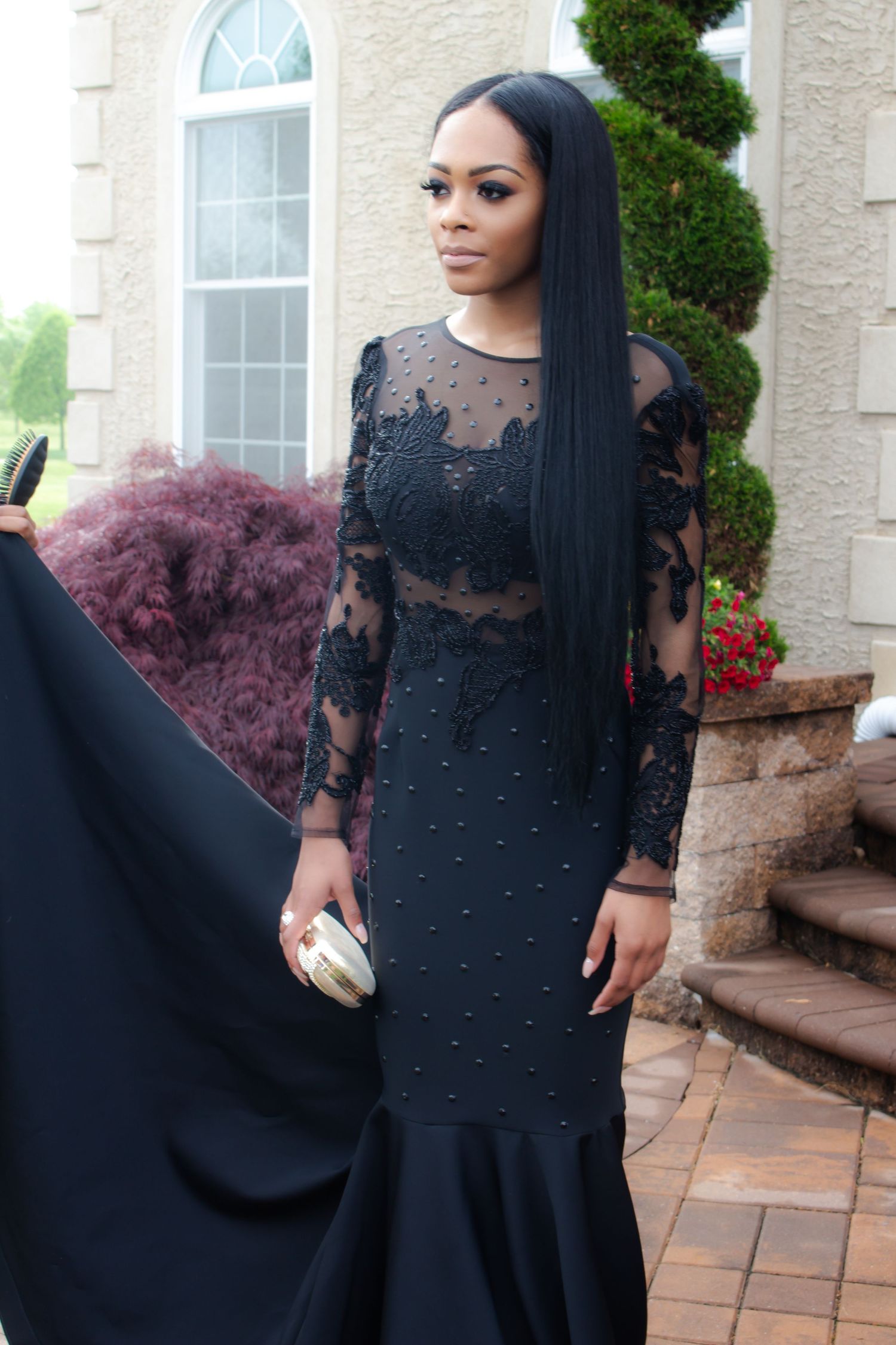 Elegant woman wearing black lace formal dress stands on outdoor stone staircase. Prom photoshoot. L. Visions Photography