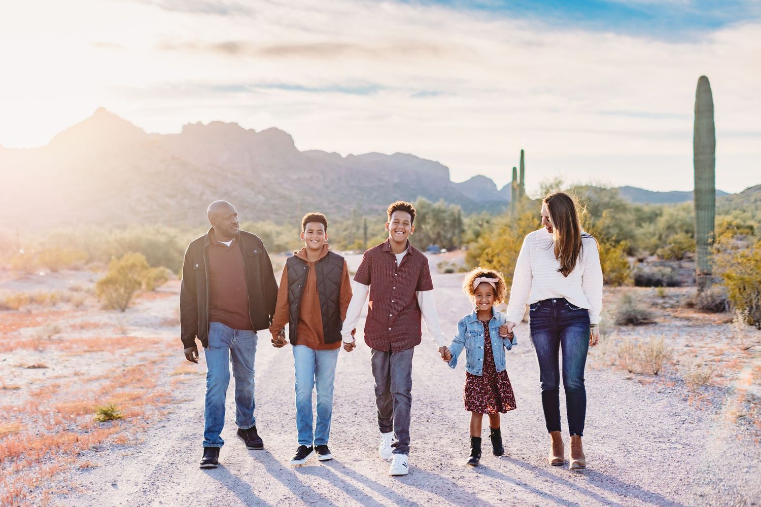 Family walking together through a desert landscape with mountains and cacti in the background at sunset.