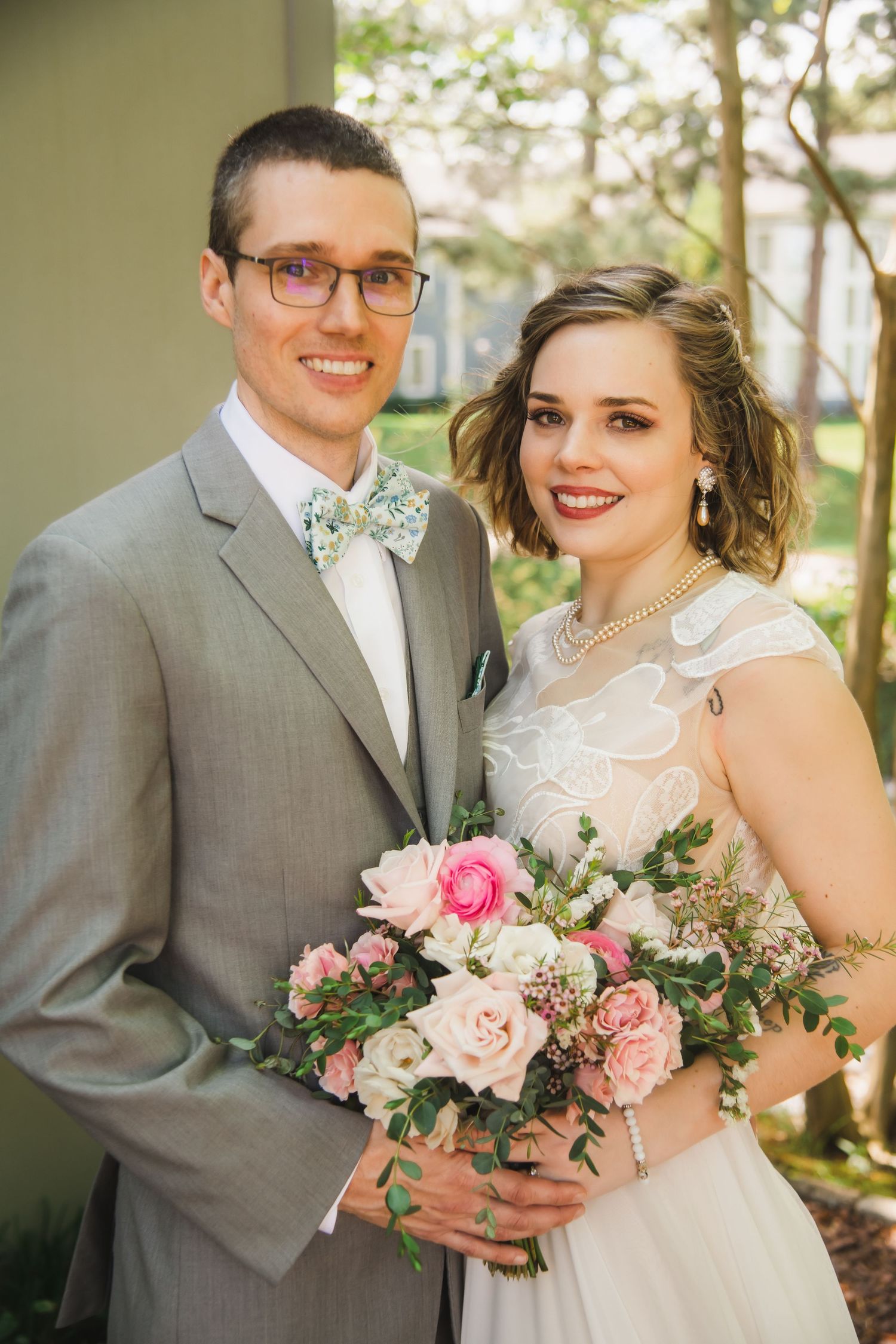 A couple in wedding attire poses with a beautiful pink and blush rose bouquet.