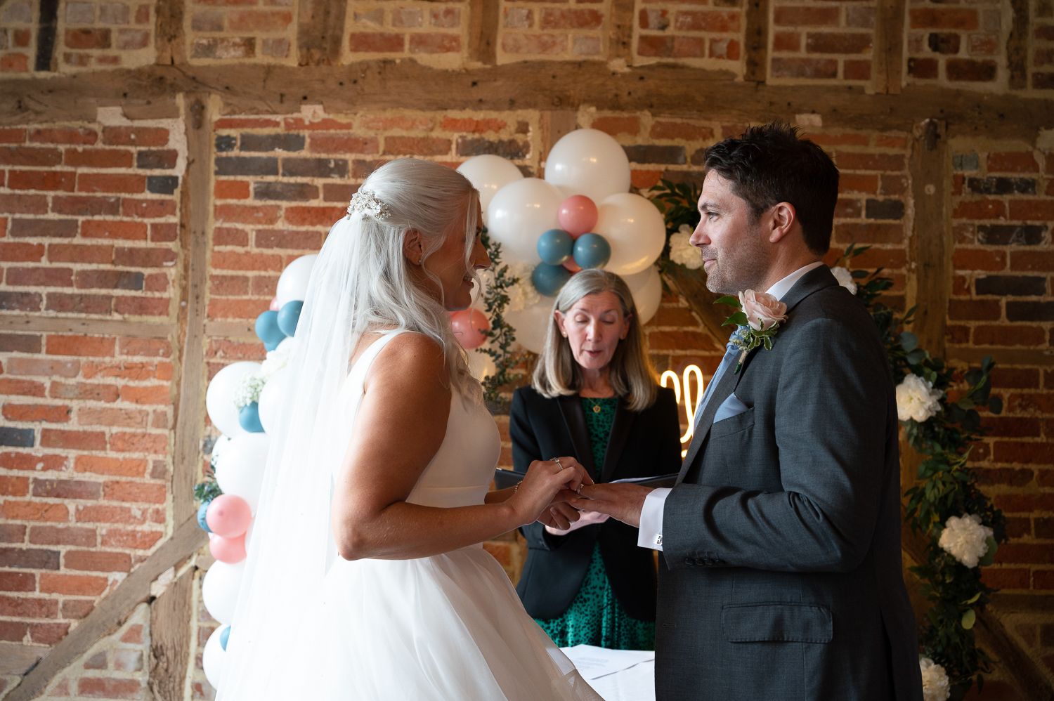 Wedding ceremony takes place in rustic brick venue with balloons and floral decorations.