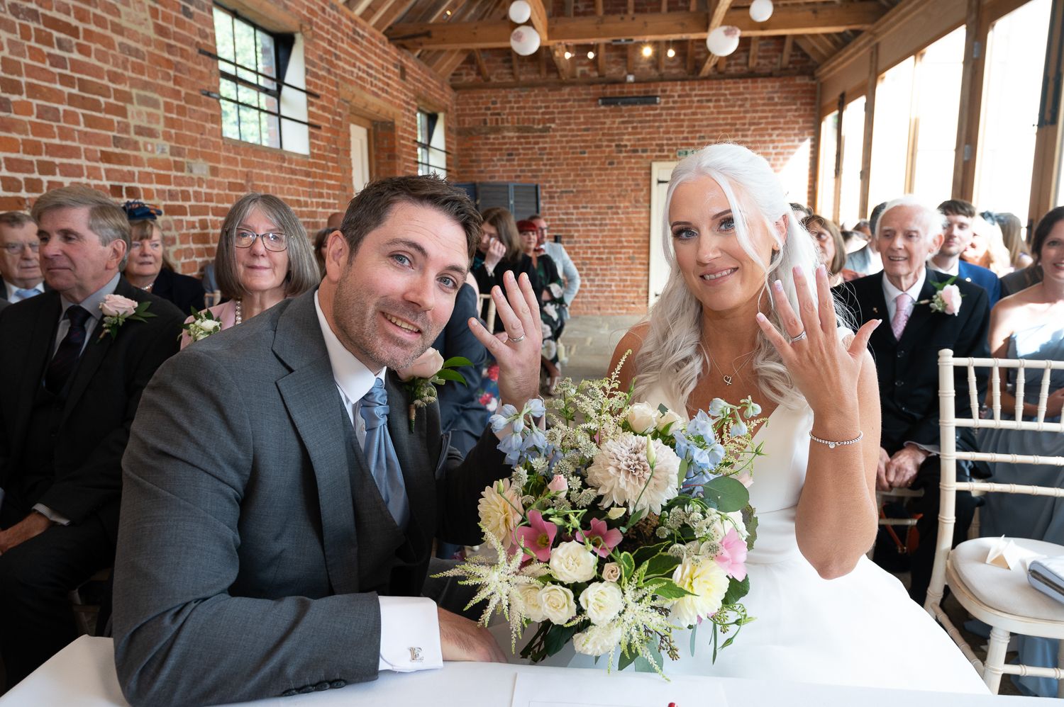 Newlyweds share joyful moment at signing table with floral bouquet.