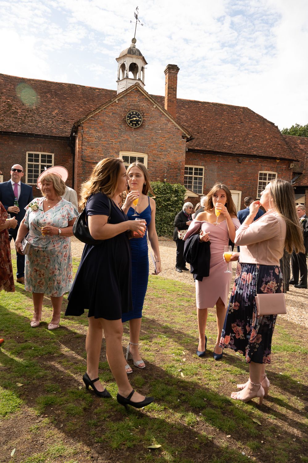 Wedding guests gathering outside historic brick building with clock tower during reception.