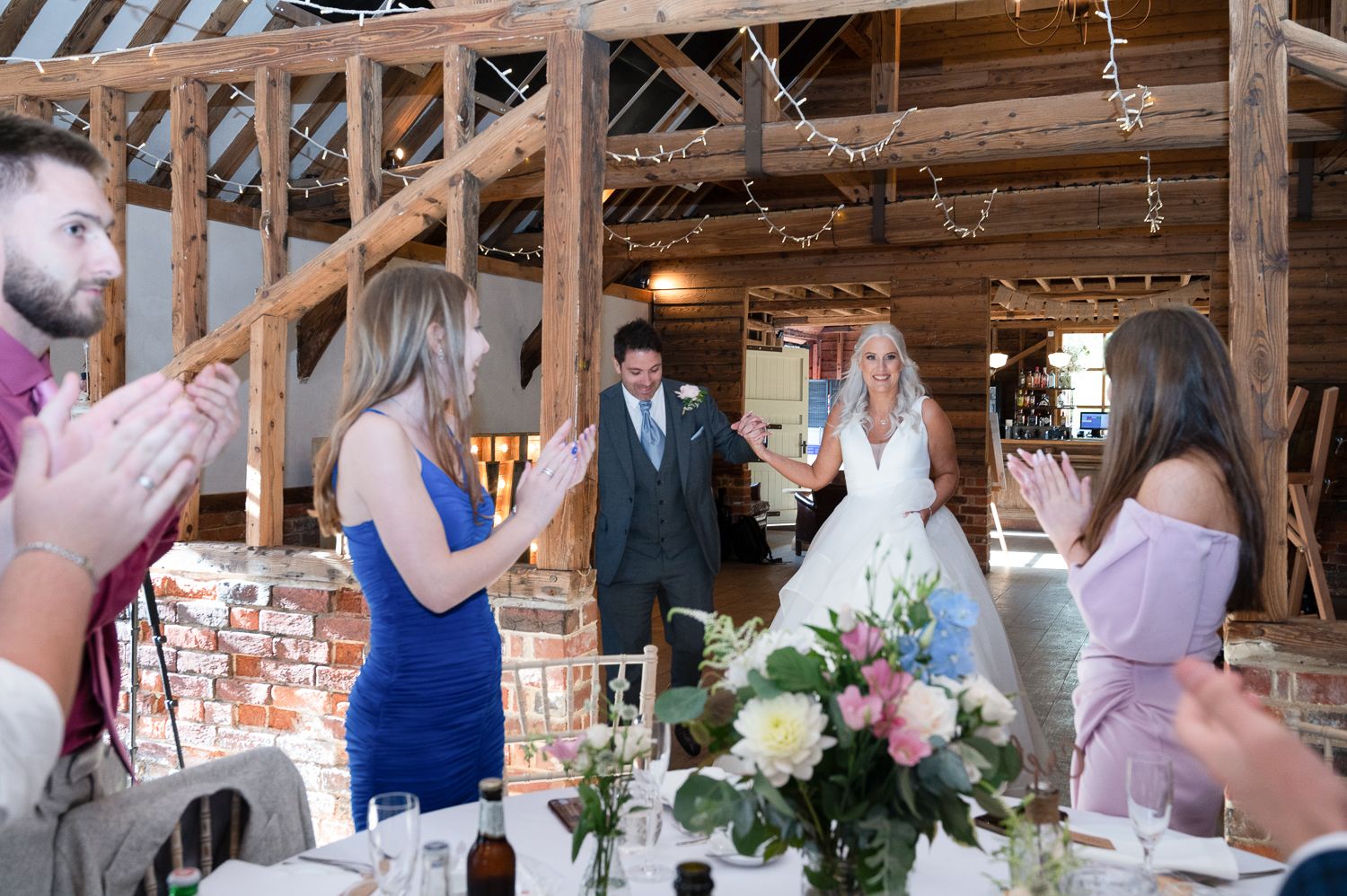 Wedding reception celebration in rustic barn venue with exposed beams and string lights.