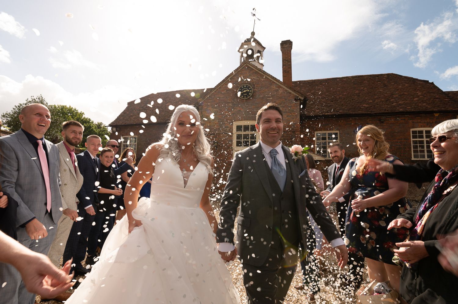 Joyful wedding celebration with guests throwing confetti outside brick church building.
