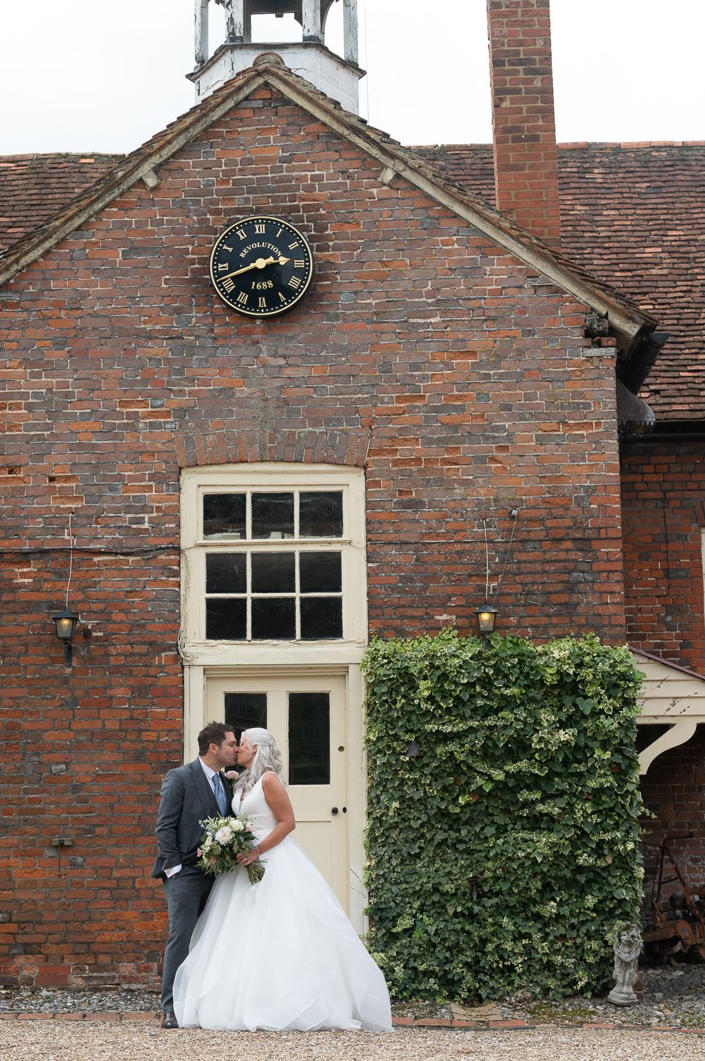 Wedding portrait in front of historic brick building with clock tower and ivy-covered walls.