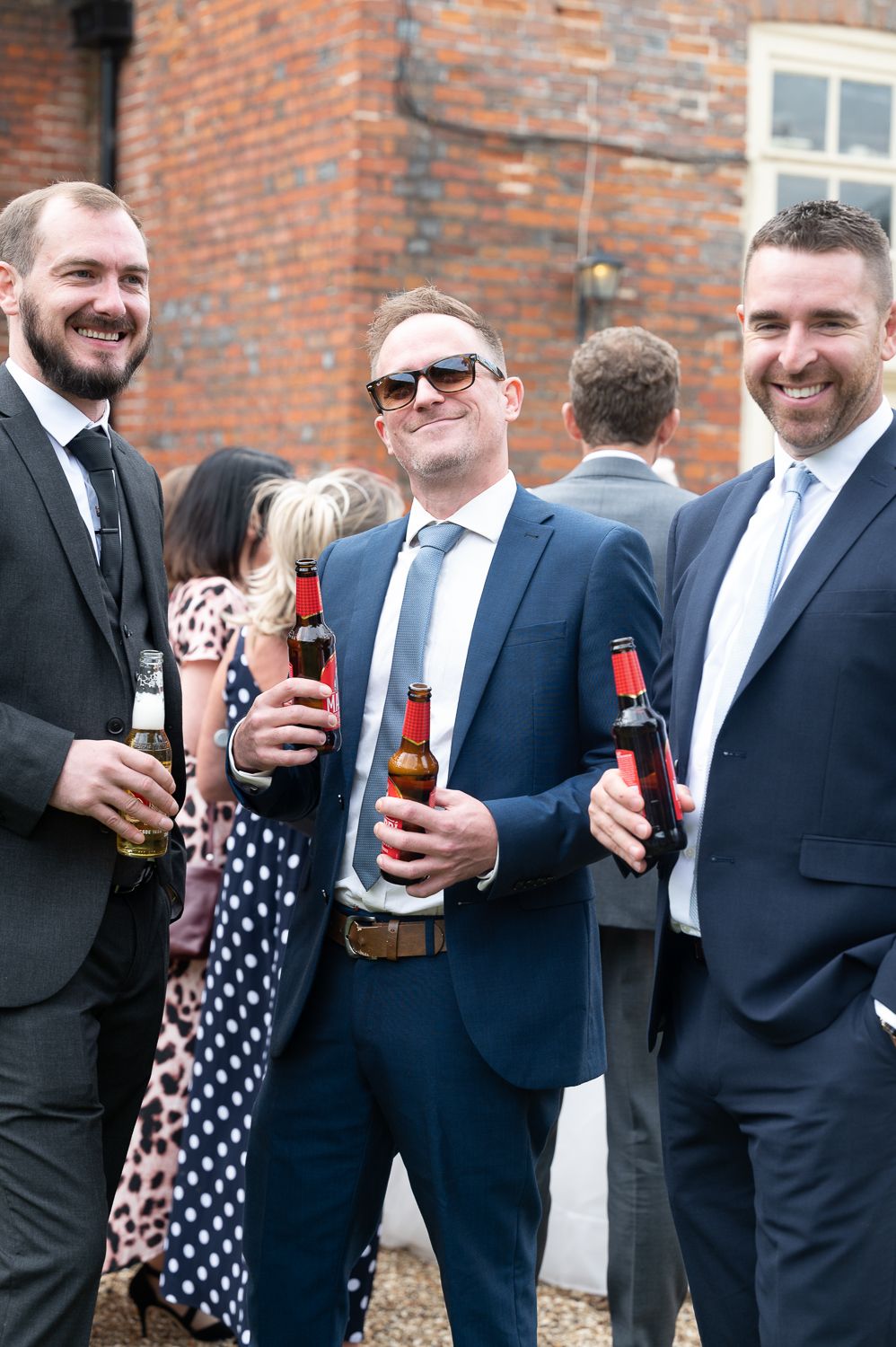 Wedding guests enjoying drinks and conversation outside brick venue.