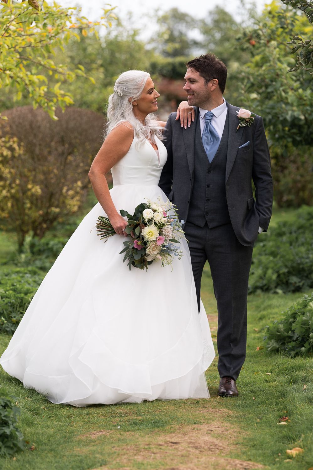 Romantic wedding portrait of couple in garden setting with lush greenery.