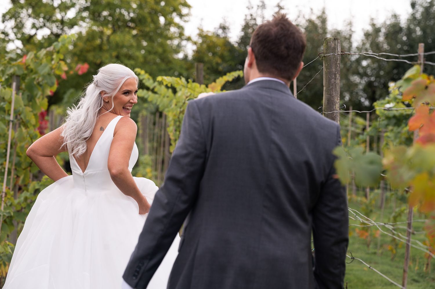 Newlyweds walk through a vineyard on their wedding day with the bride's dress flowing behind.