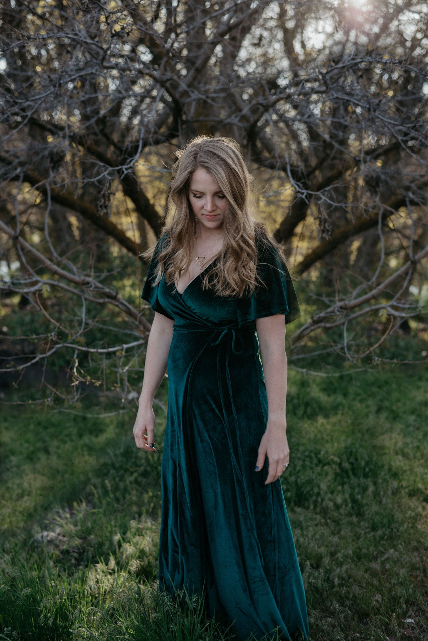 portrait of a woman in a baltic born dress looks down with a tree behind her during sunset
