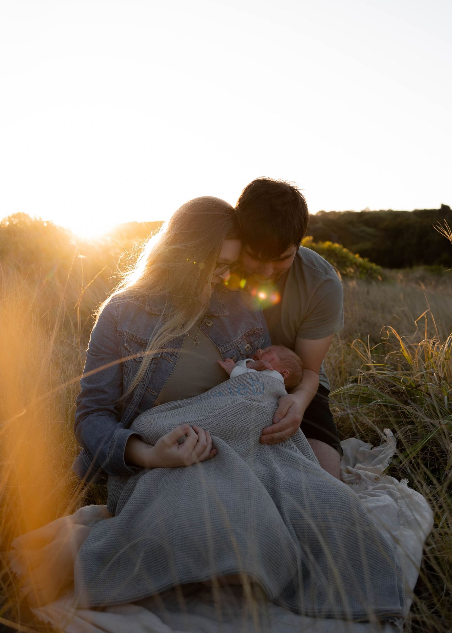 Mum, dad and their newborn baby sharing a peaceful moment in a grassy hill in the sunshine. Family outdoor photoshoot in the Illawarra.
