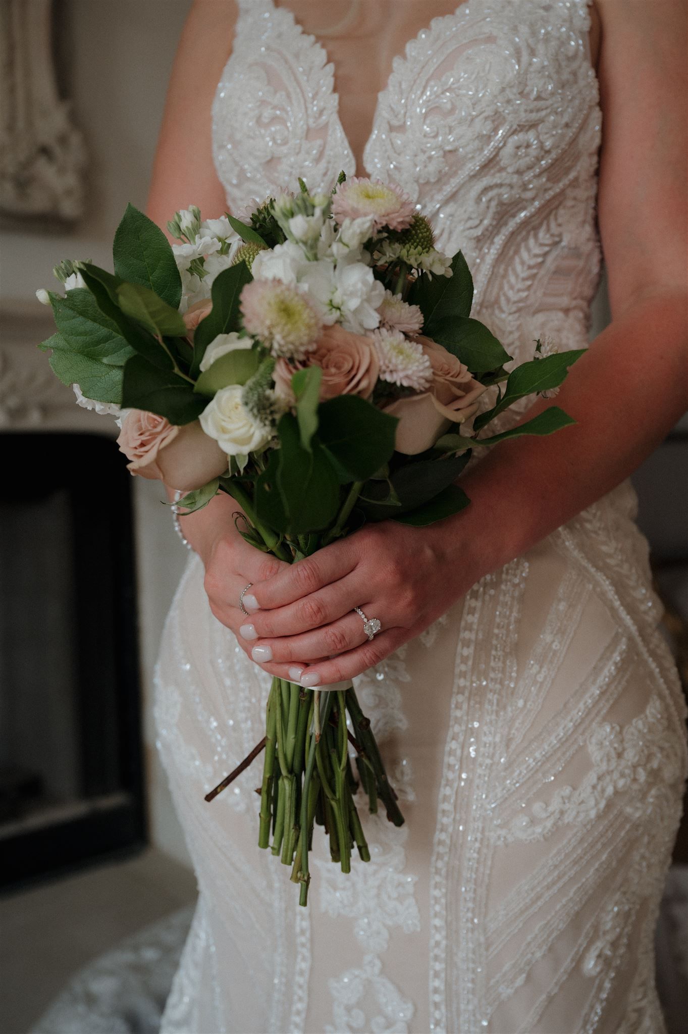 Close-up of bridal bouquet with white flowers and greenery against lace wedding dress.