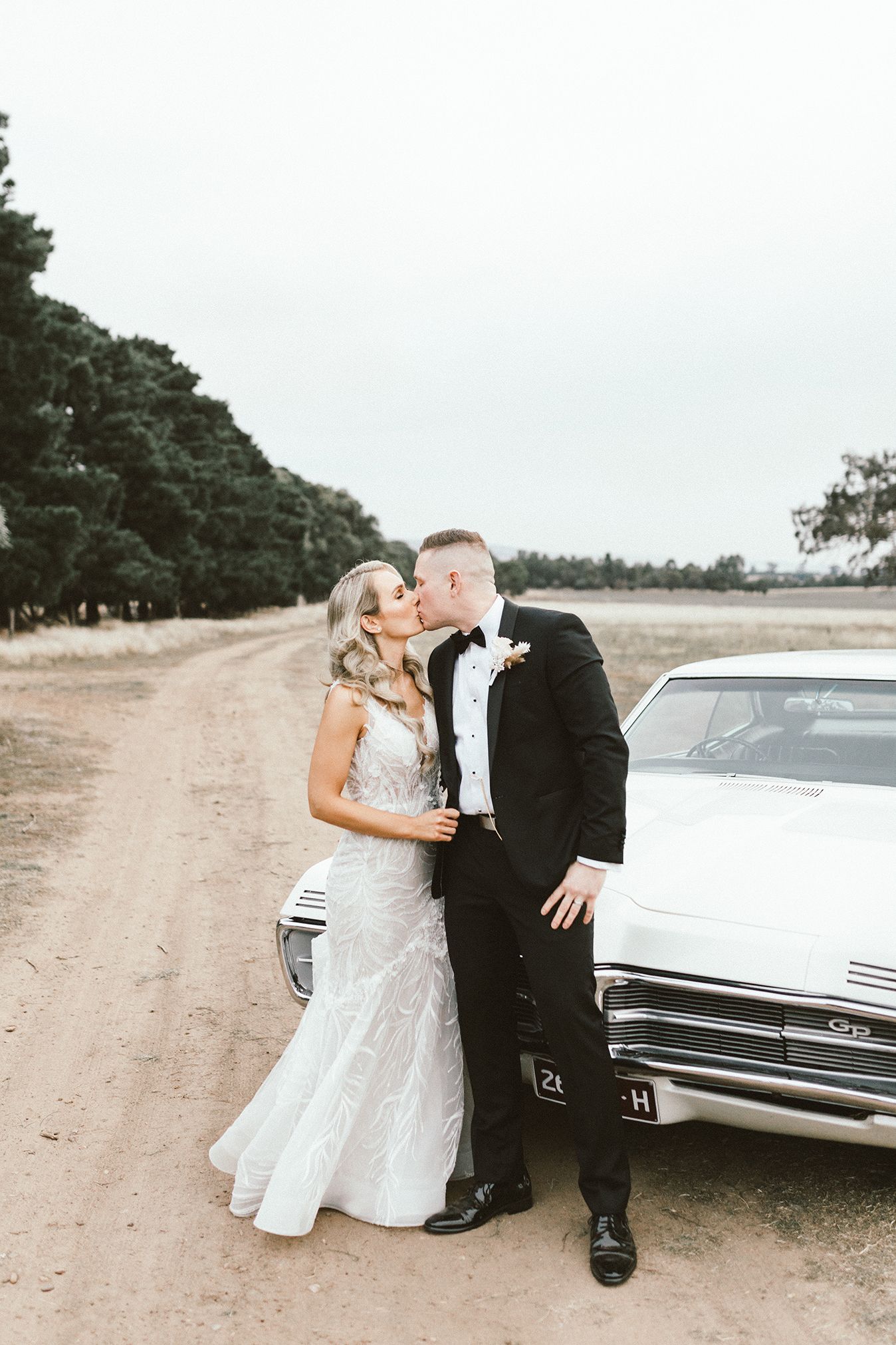 A romantic wedding portrait with a classic car on a country road.