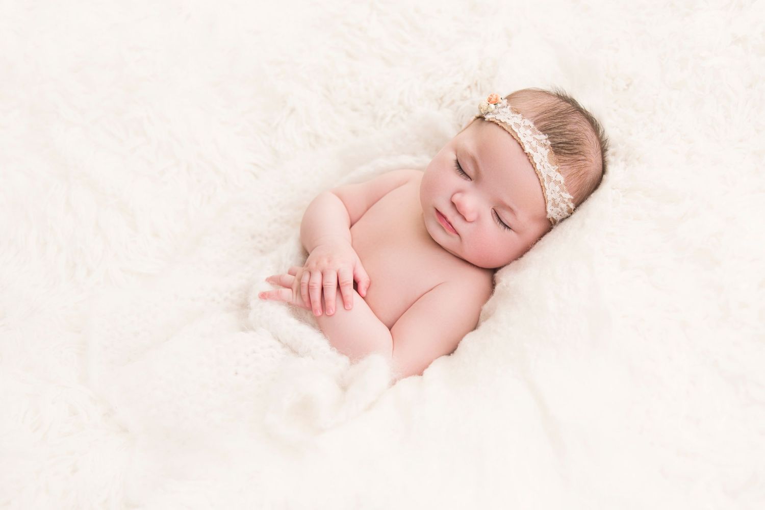 Sleeping baby on white fluffy blanket during newborn photo session.