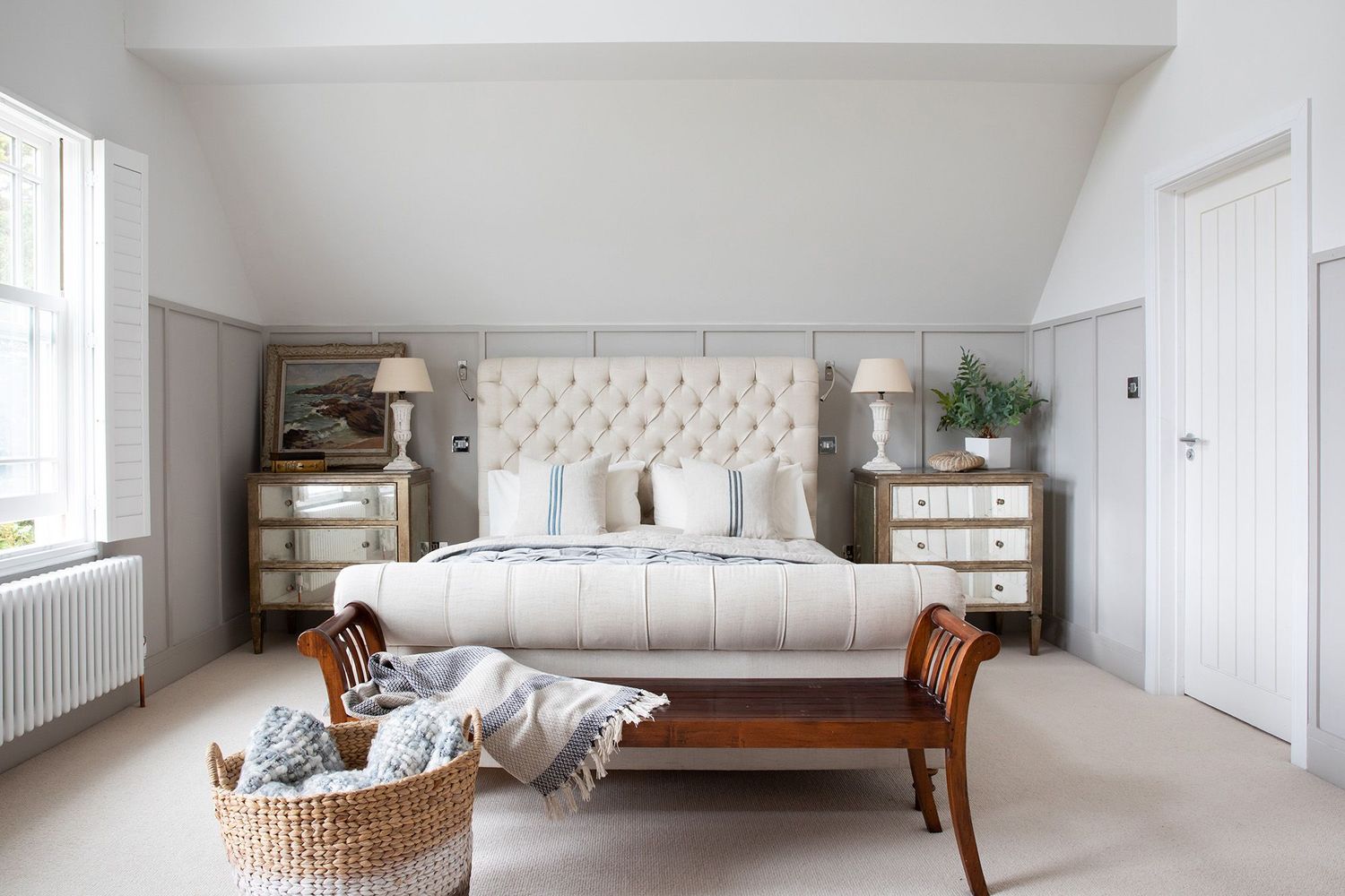 Luxurious bedroom with tufted headboard, wooden bench, and mirrored nightstands in neutral tones.