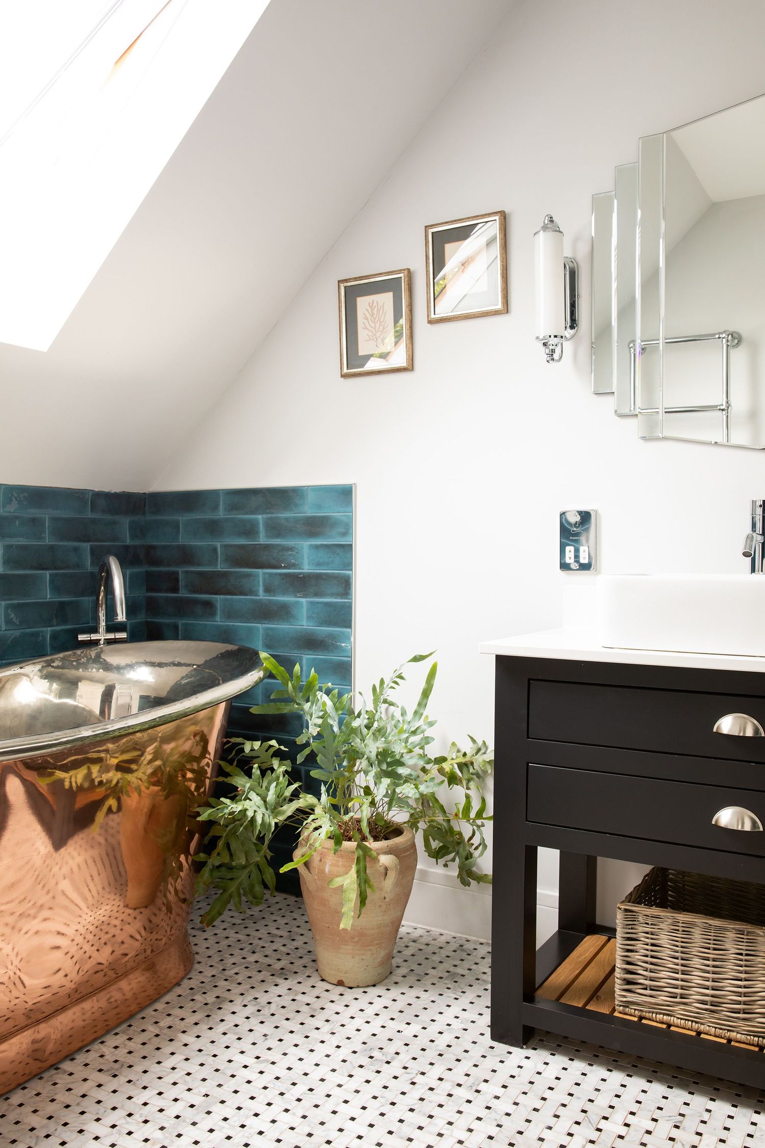 Elegant bathroom with copper tub, black vanity, and teal tile backsplash under sloped ceiling.