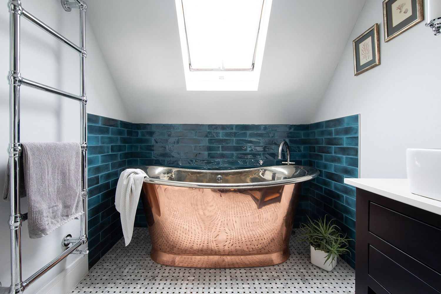 Attic bathroom featuring copper freestanding tub against teal subway tile with skylight above.