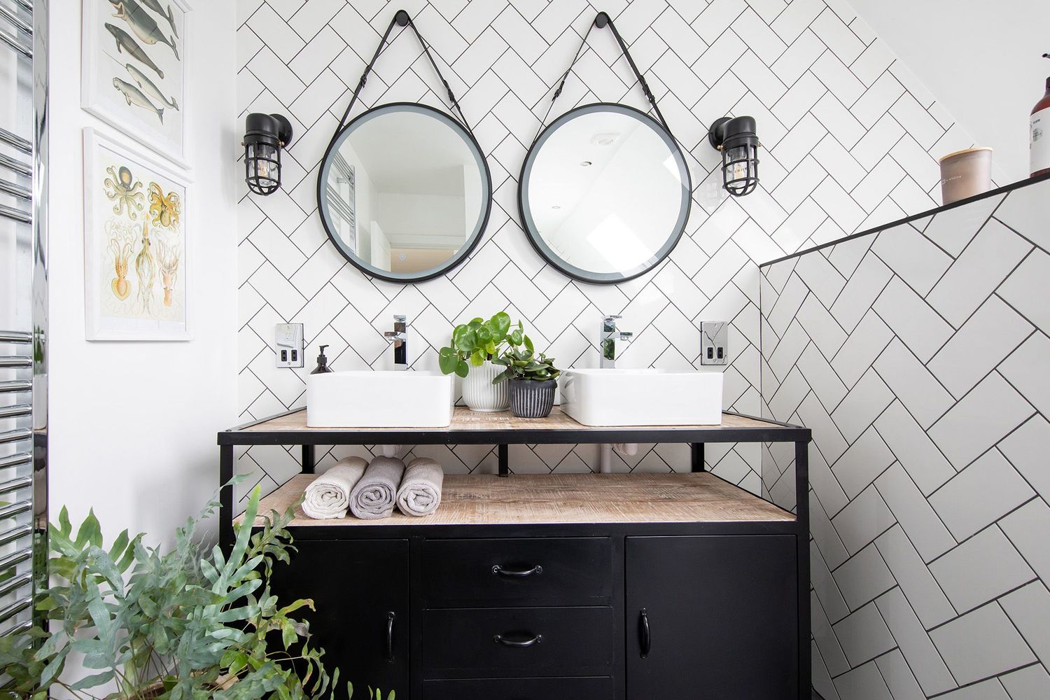 Modern bathroom with dual round mirrors, black vanity, and white herringbone tile backsplash.