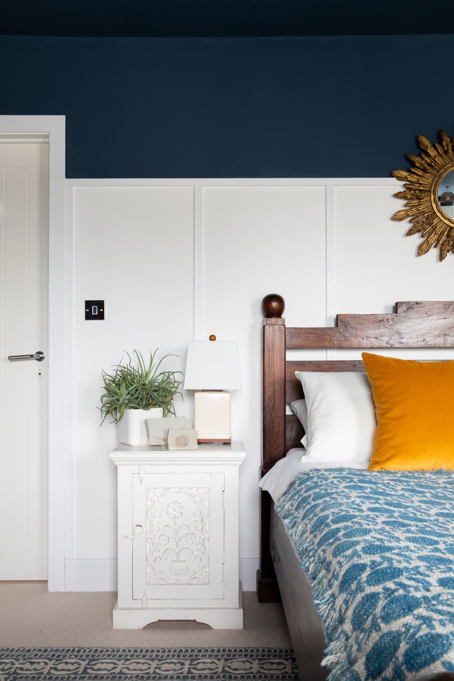 Cozy bedroom with dark blue walls, wooden bed frame, blue patterned bedding, and orange accent pillow.