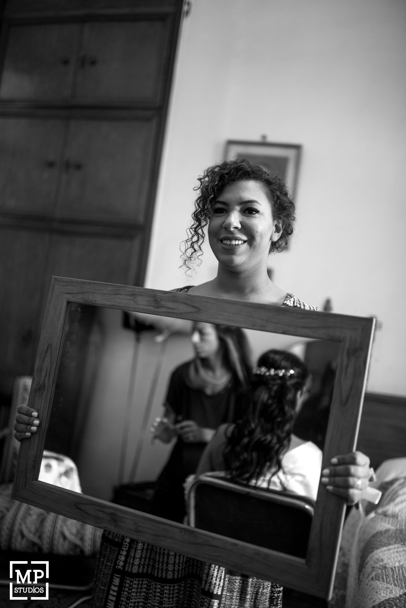A black and white photo shows someone with curly hair holding up a mirror to create a reflection.
