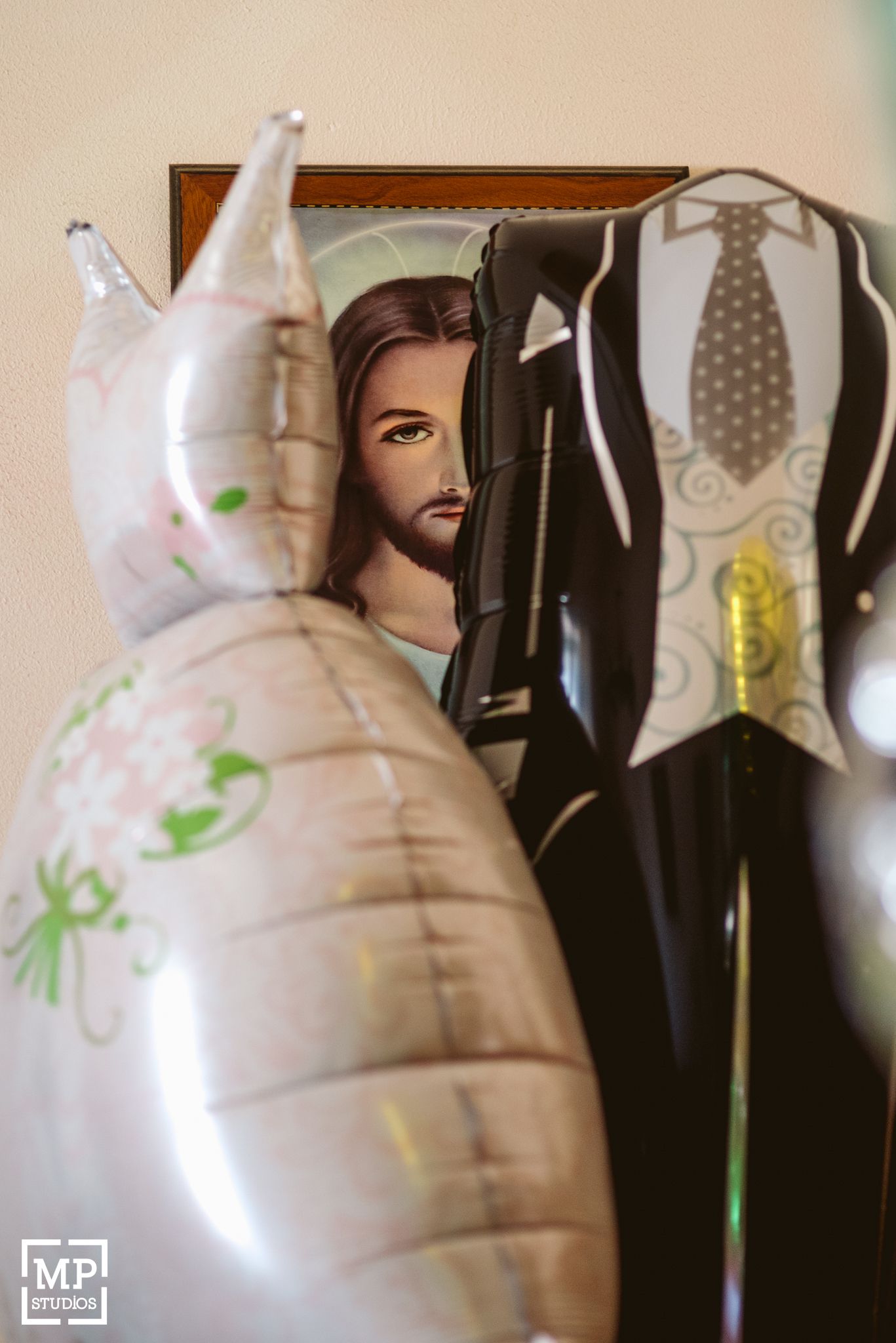 Religious artwork and wedding decorations including silver balloons displayed against a wall.