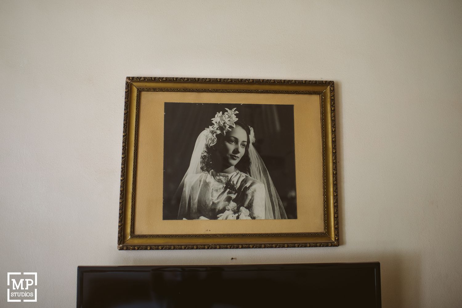 Vintage wedding portrait in ornate gold frame hanging on wall.
