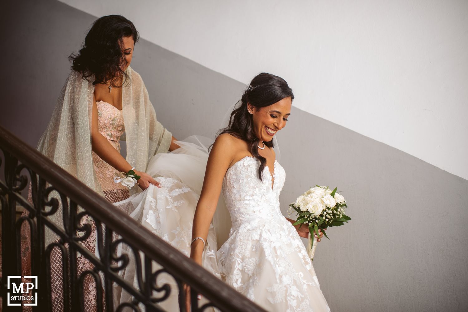 Wedding party descending an elegant staircase in flowing white dresses.