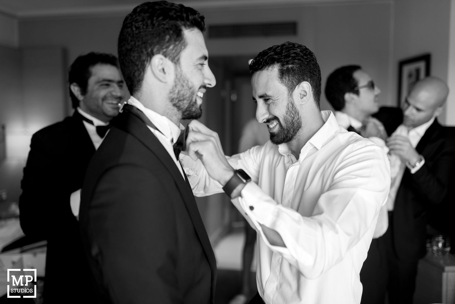 Two men in formal attire adjusting each other's bow ties.