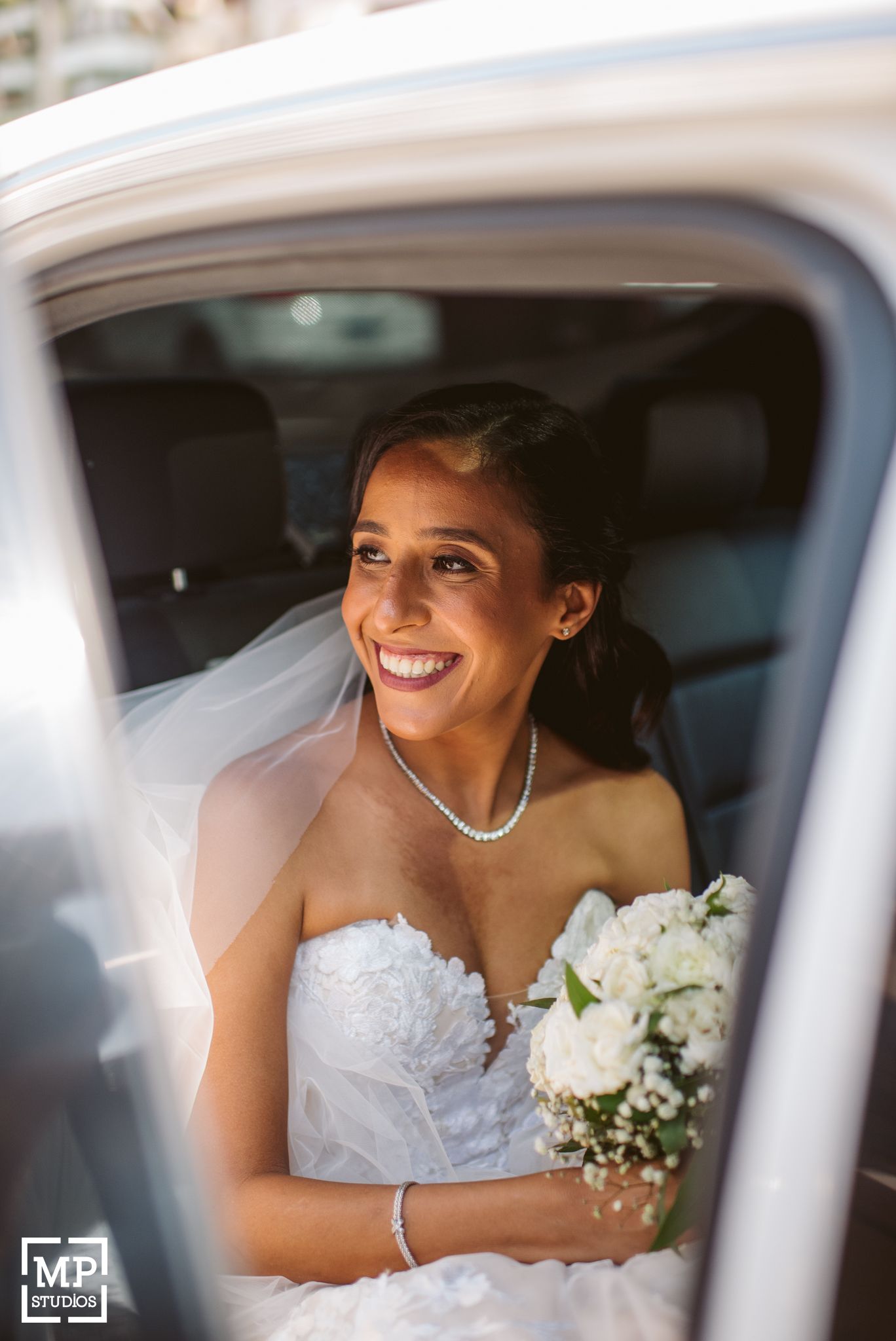 Person in white wedding dress smiling radiantly in car window.