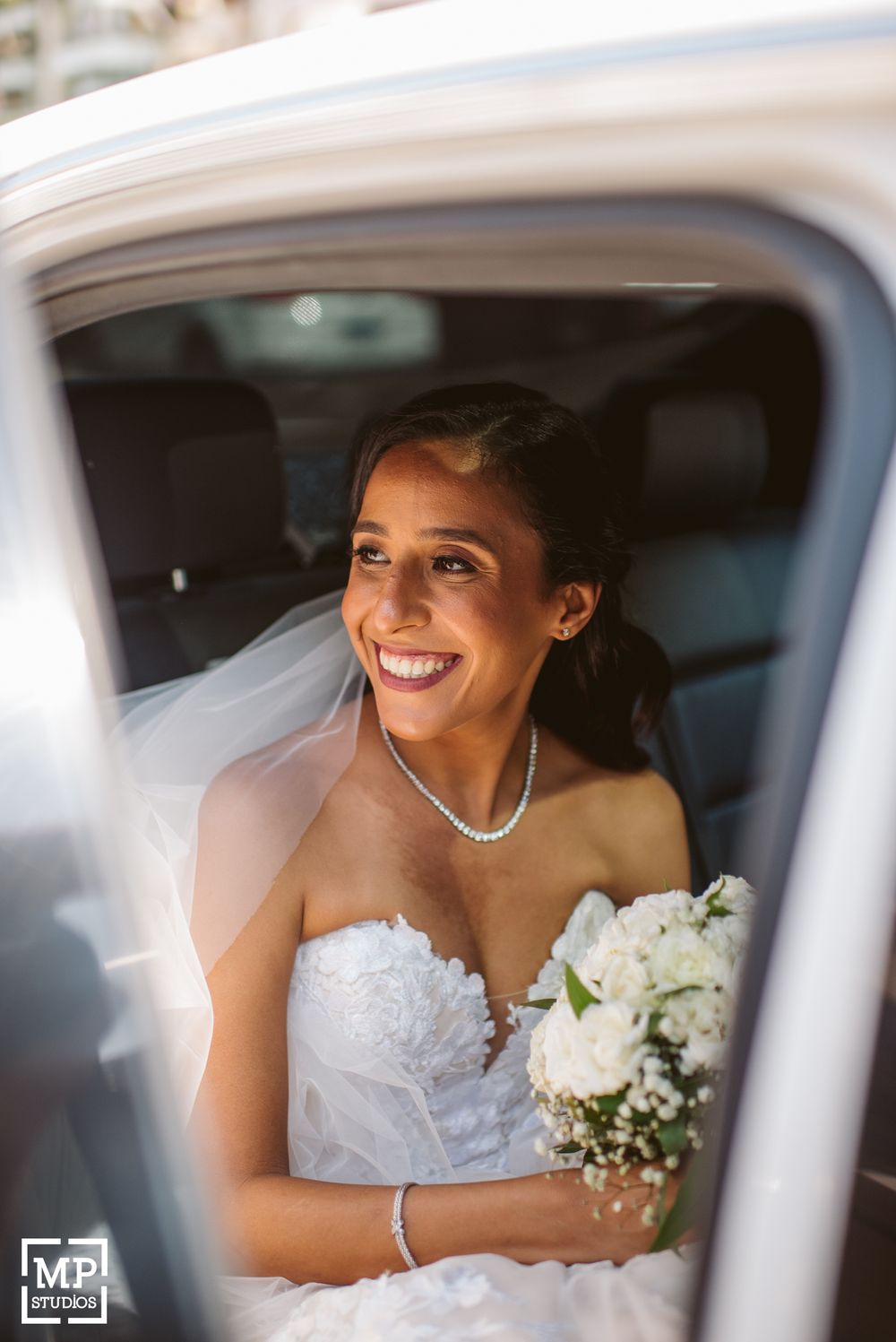 Person in white wedding dress smiling radiantly in car window.