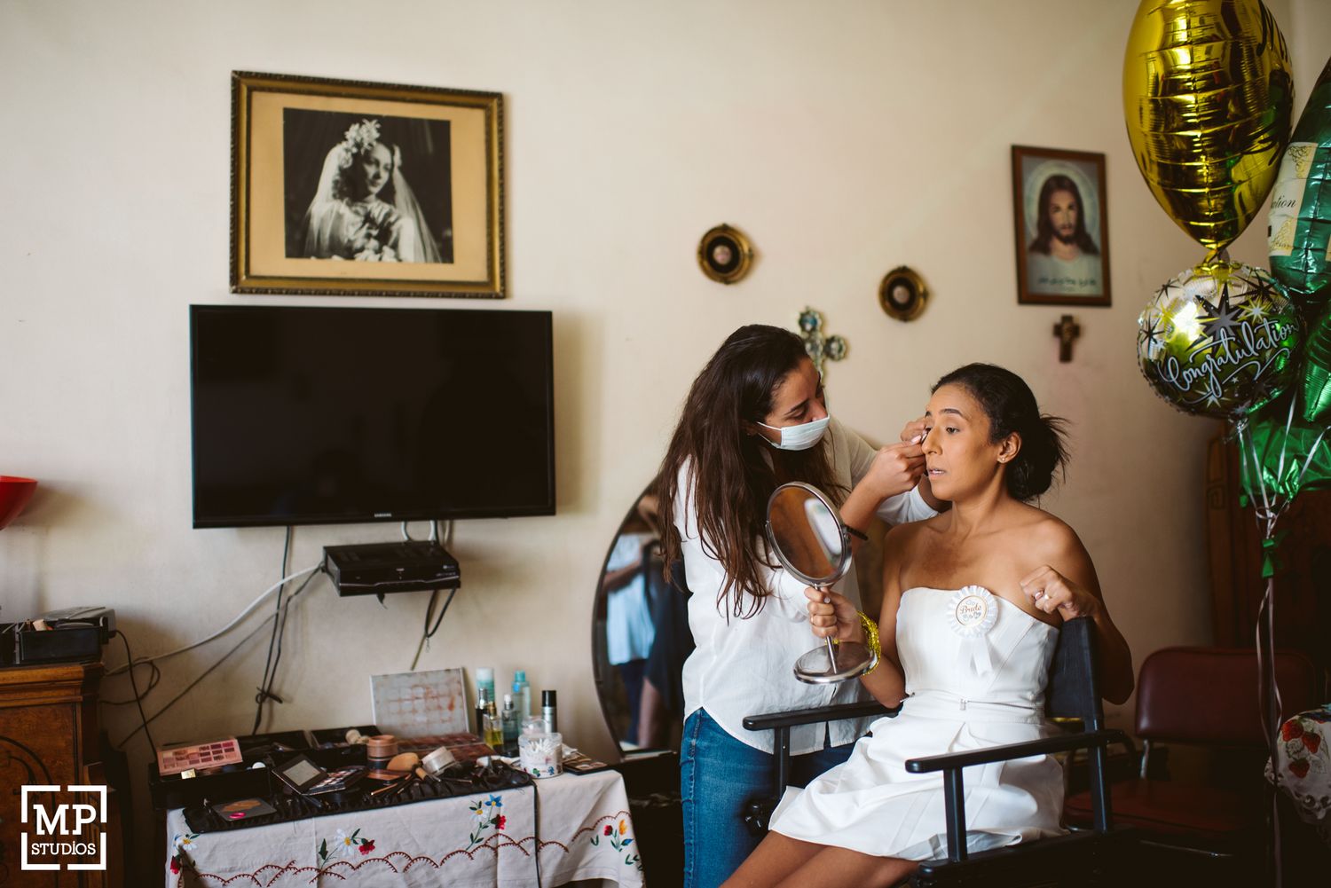 Wedding preparation scene with makeup application in room with framed photos and balloons.