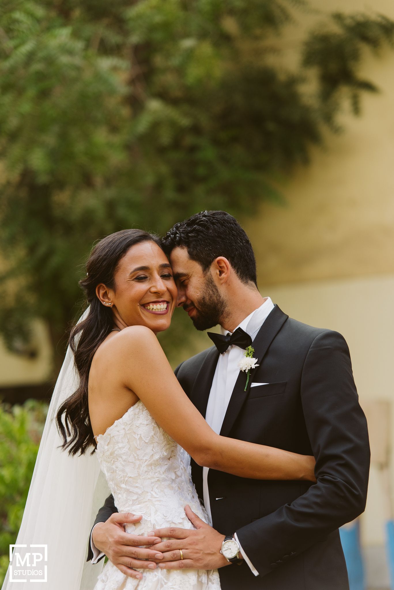 Romantic wedding portrait of a couple embracing outdoors in formal attire.