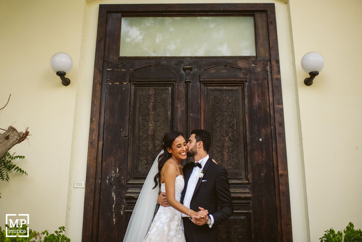 Romantic wedding portrait in front of vintage wooden door with ornate architectural details.