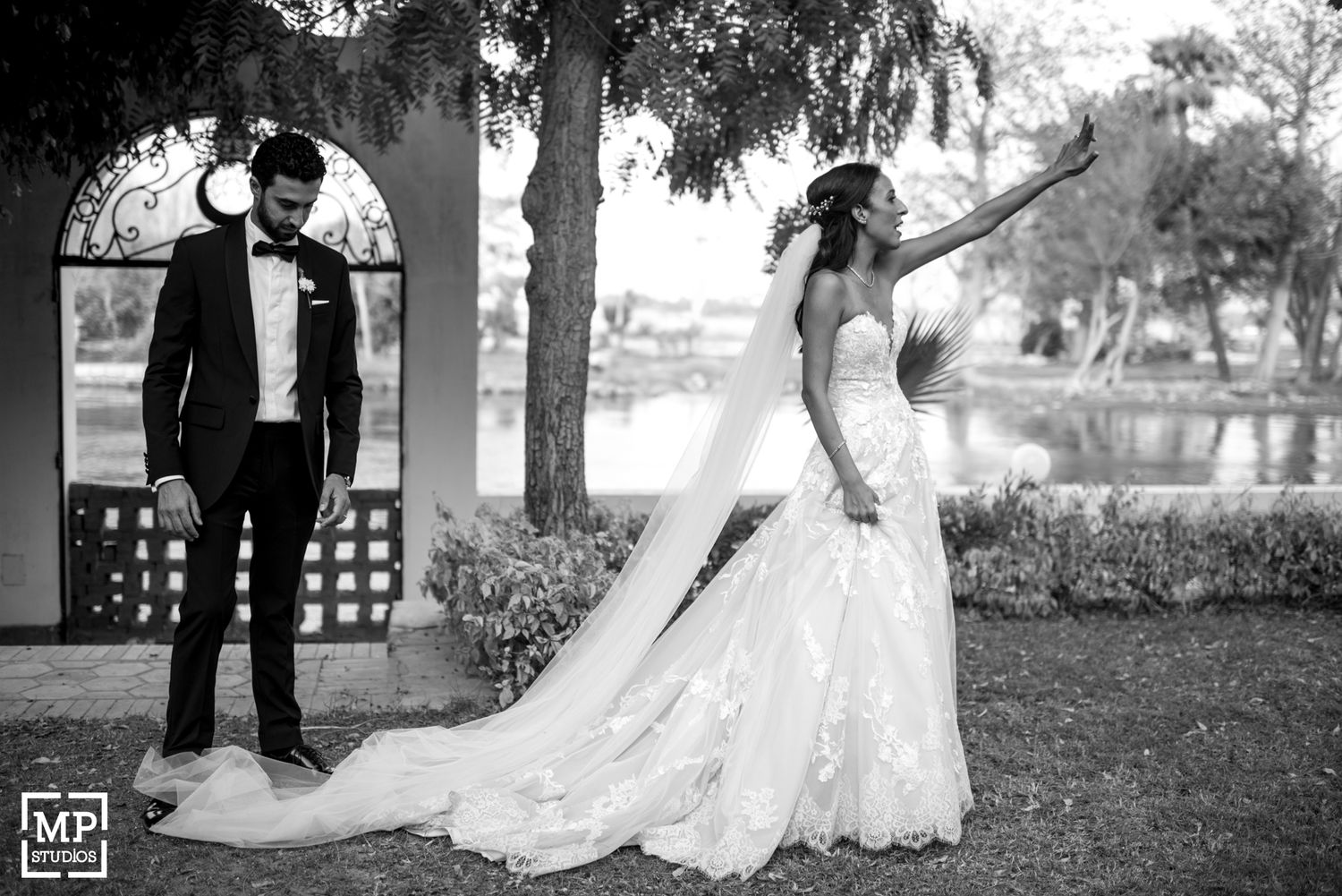 Dramatic black and white wedding photo with flowing lace dress against arched garden backdrop.