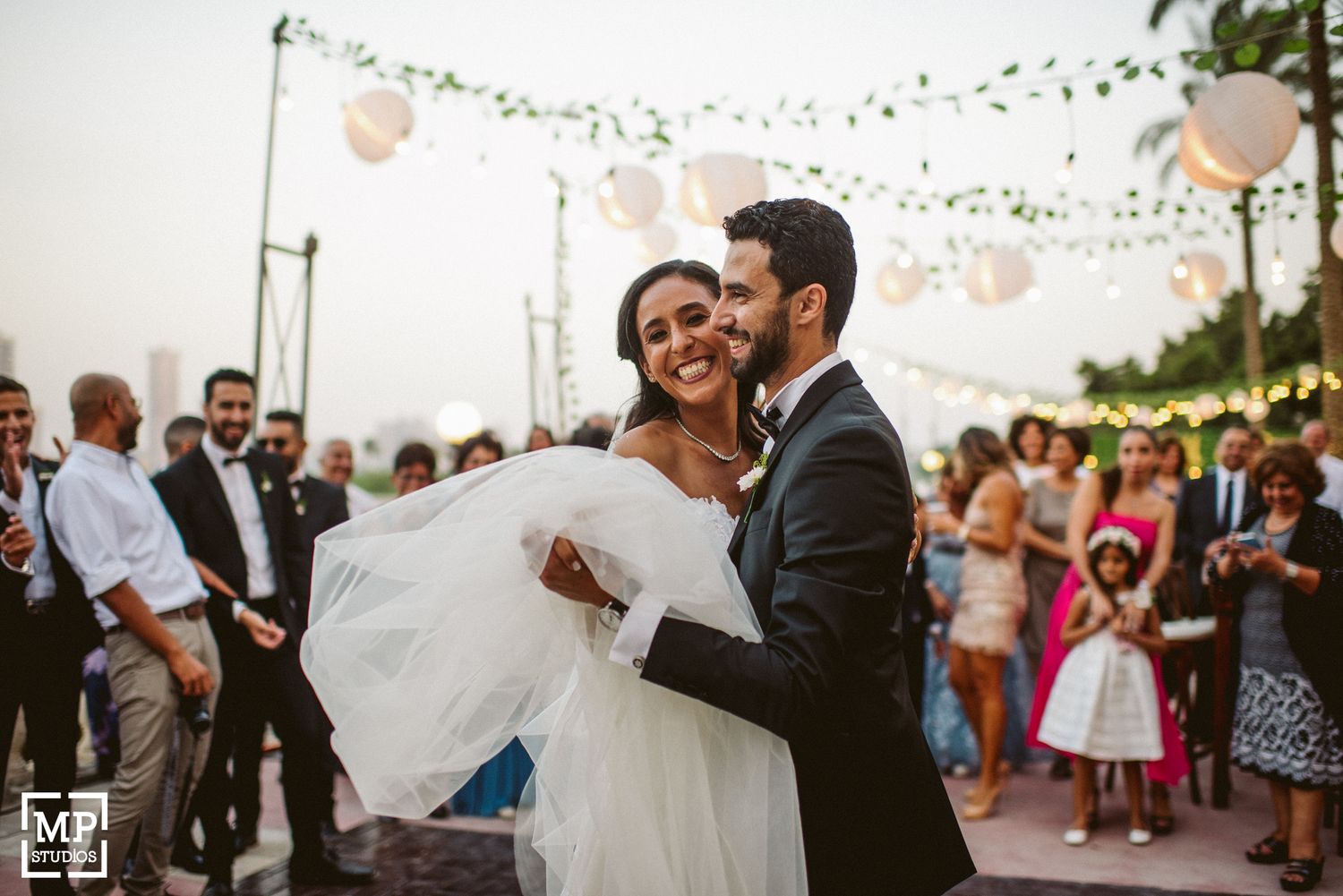 Joyful moment during outdoor wedding reception under string lights and lanterns.