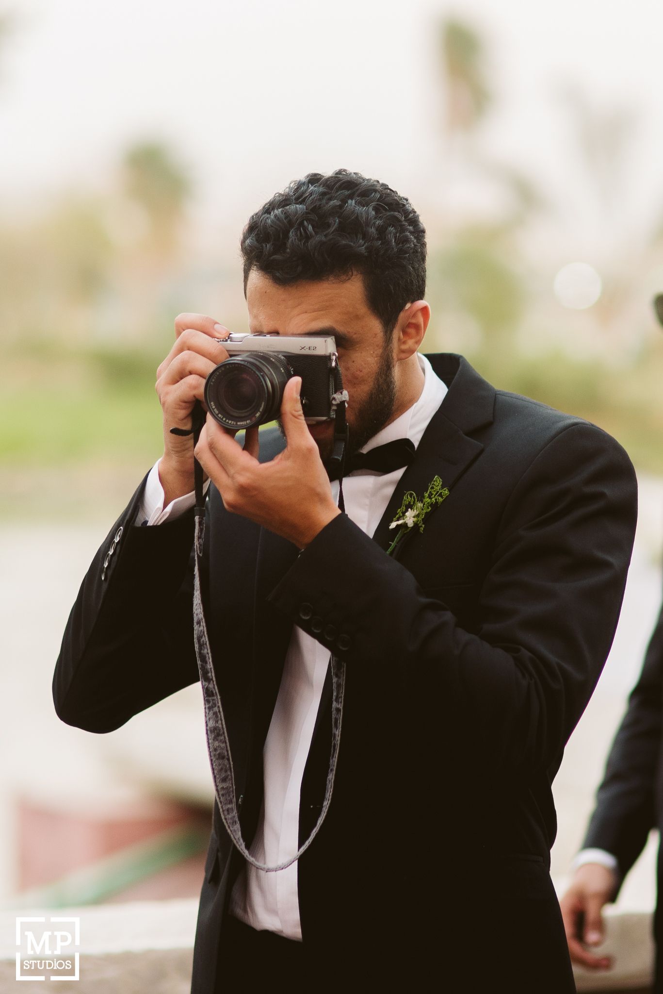 Person in formal black tuxedo taking a photograph with vintage camera.