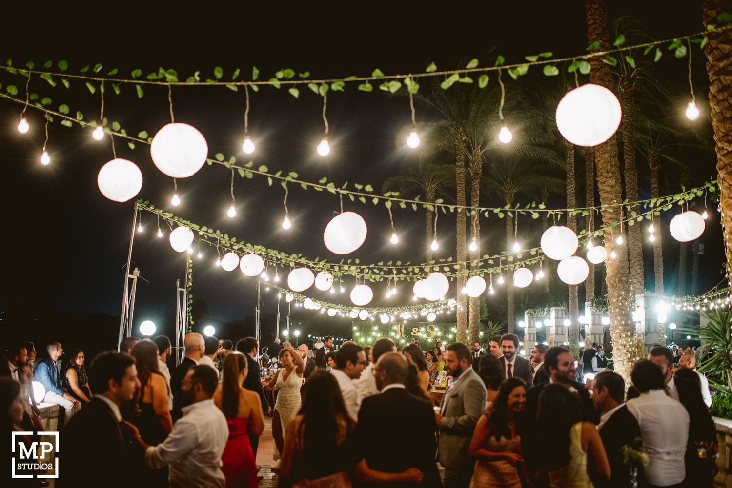 Outdoor evening wedding reception with string lights and paper lanterns creating a magical atmosphere.