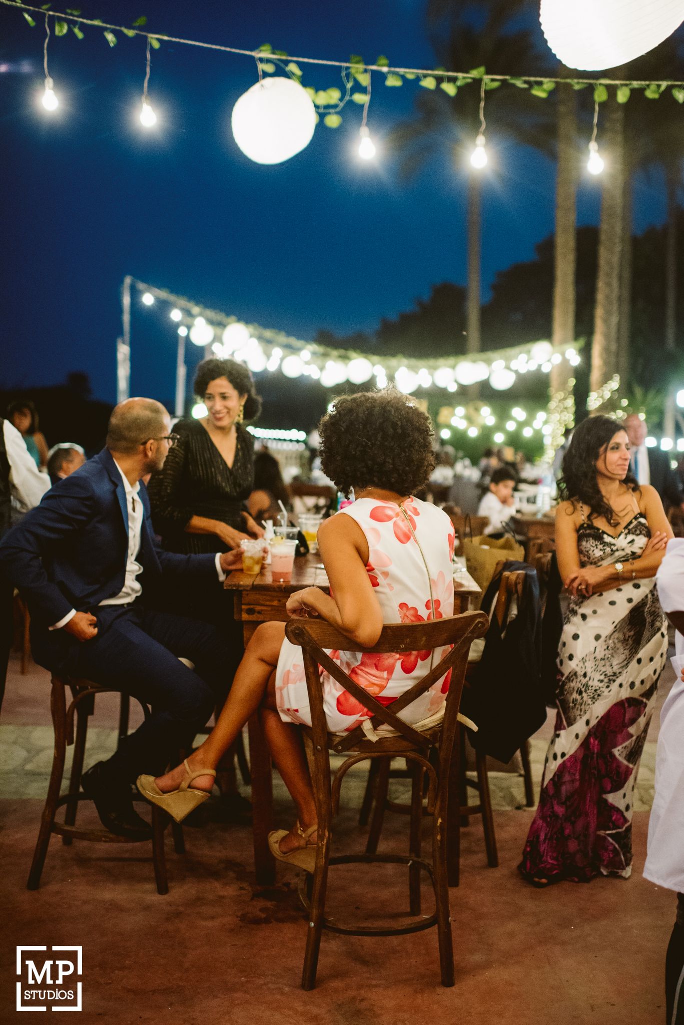 Guests enjoying an intimate outdoor dinner under string lights and paper lanterns at dusk.