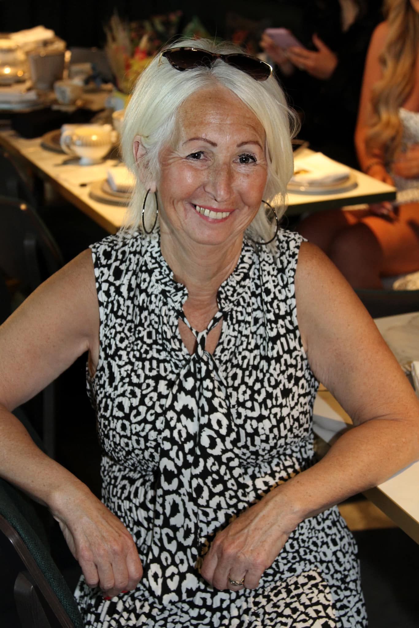 Woman in black and white patterned dress seated at dining table during social event.