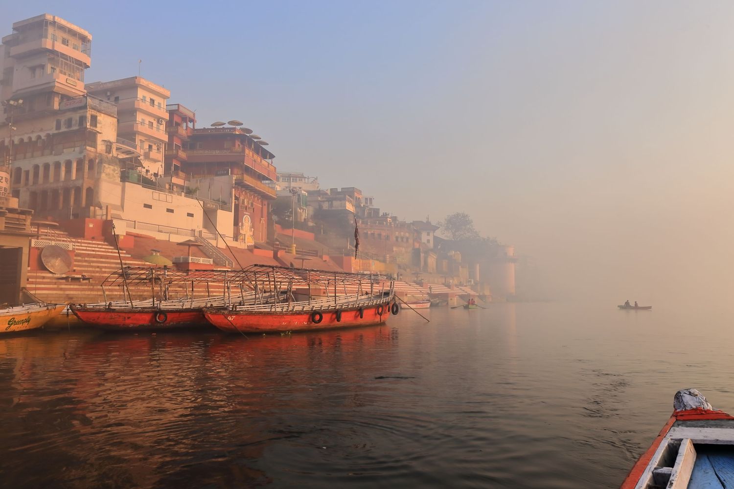 Misty morning view of boats and buildings along the Ganges River in Varanasi, India.