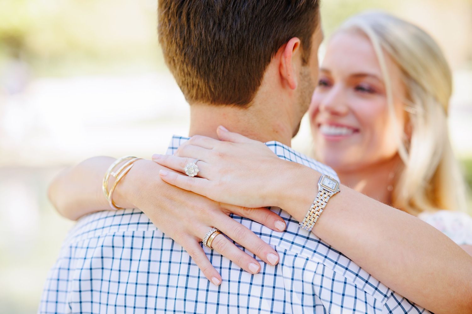 Engaged couple embraces outdoors while showing off a sparkling diamond ring.