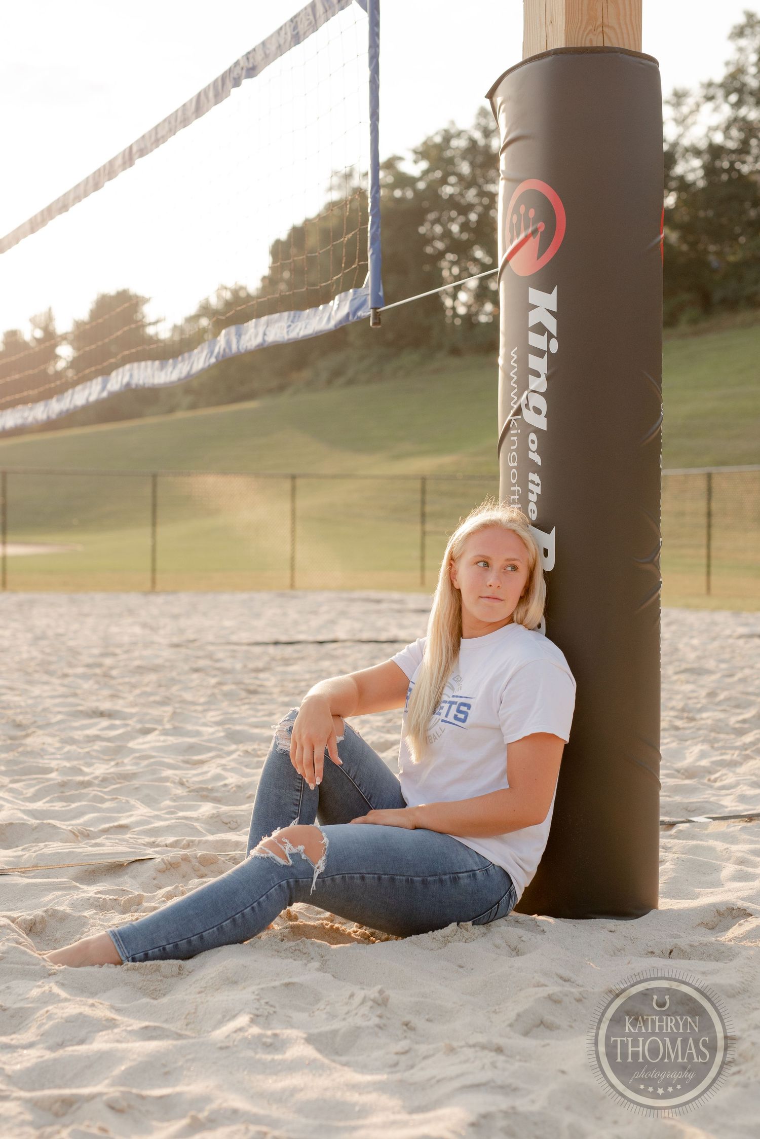 Athlete sitting on sandy volleyball court against pole during golden hour sunset.