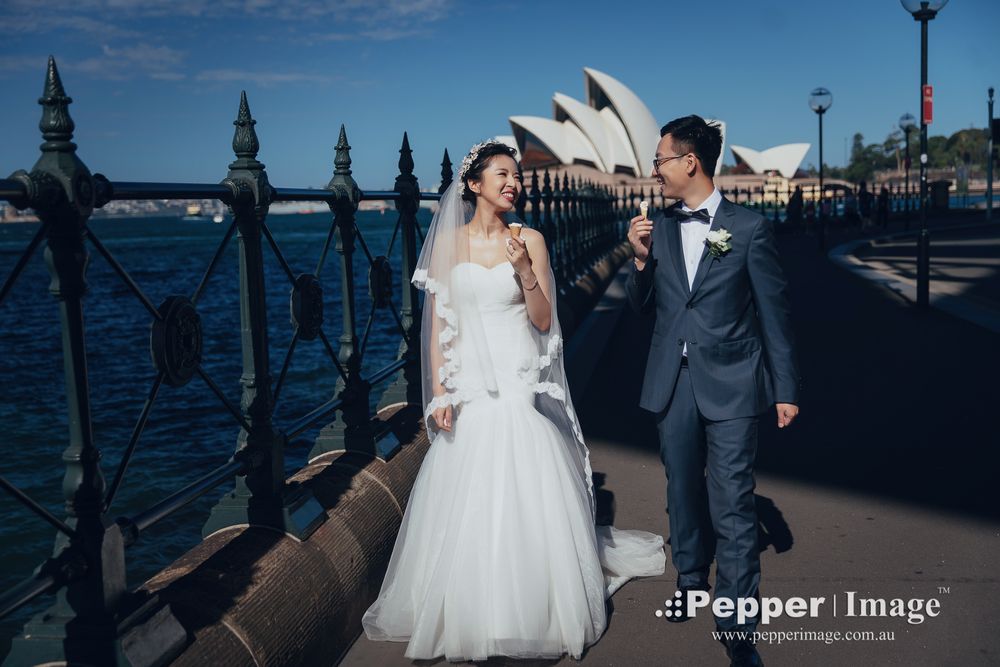 Bride and groom posing happily by Sydney Harbour with Opera House in background.
