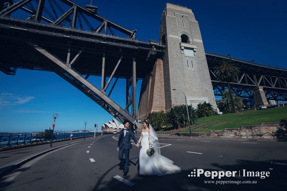 Bride and groom walking under Sydney Harbour Bridge on empty road on wedding day.