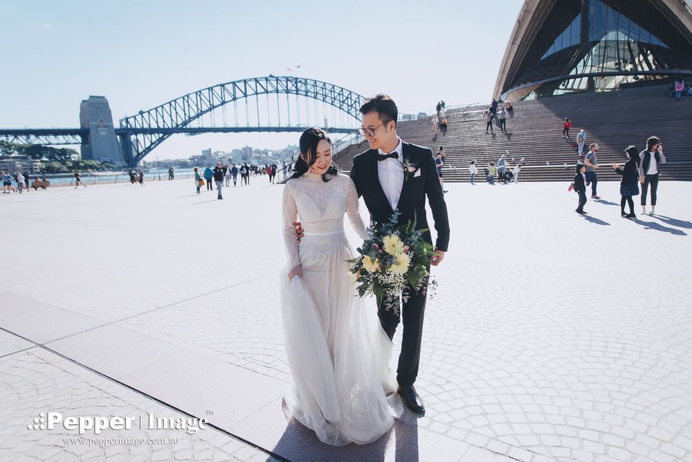 Wedding couple walking hand in hand with Sydney Harbour Bridge backdrop on sunny day.